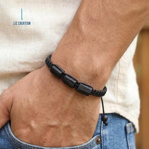 May include: Black beaded bracelet with three rectangular stones and a woven cord. The bracelet is worn on a wrist, with the text "LIZ CREATION" visible in the background.