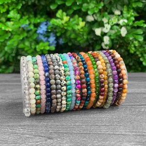 Op de afbeelding: Een stapel kleurrijke kralenarmbanden gemaakt van verschillende natuurlijke stenen, waaronder amethist, turquoise en jaspis.