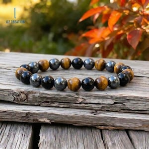 May include: A beaded bracelet featuring a mix of polished, round beads in shades of black, brown, and silver. The bracelet is displayed on a weathered wooden surface, with a blurred natural background. The bracelet is a jewelry item.