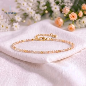 May include: A delicate bracelet featuring small, faceted, light peach-colored gemstone beads interspersed with tiny, polished gold-tone metal spheres. The piece includes a gold-tone lobster claw clasp, an adjustable chain, and a small heart-shaped charm.