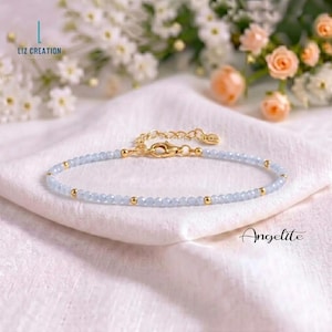 Könnte beinhalten: Ein zartes Armband mit kleinen, hellblauen facettierten Perlen, die mit winzigen goldfarbenen Metallkugeln durchsetzt sind. Das Schmuckstück verfügt über einen goldfarbenen Karabinerverschluss und eine verstellbare Verlängerungskette mit einem kleinen herzförmigen Anhänger.