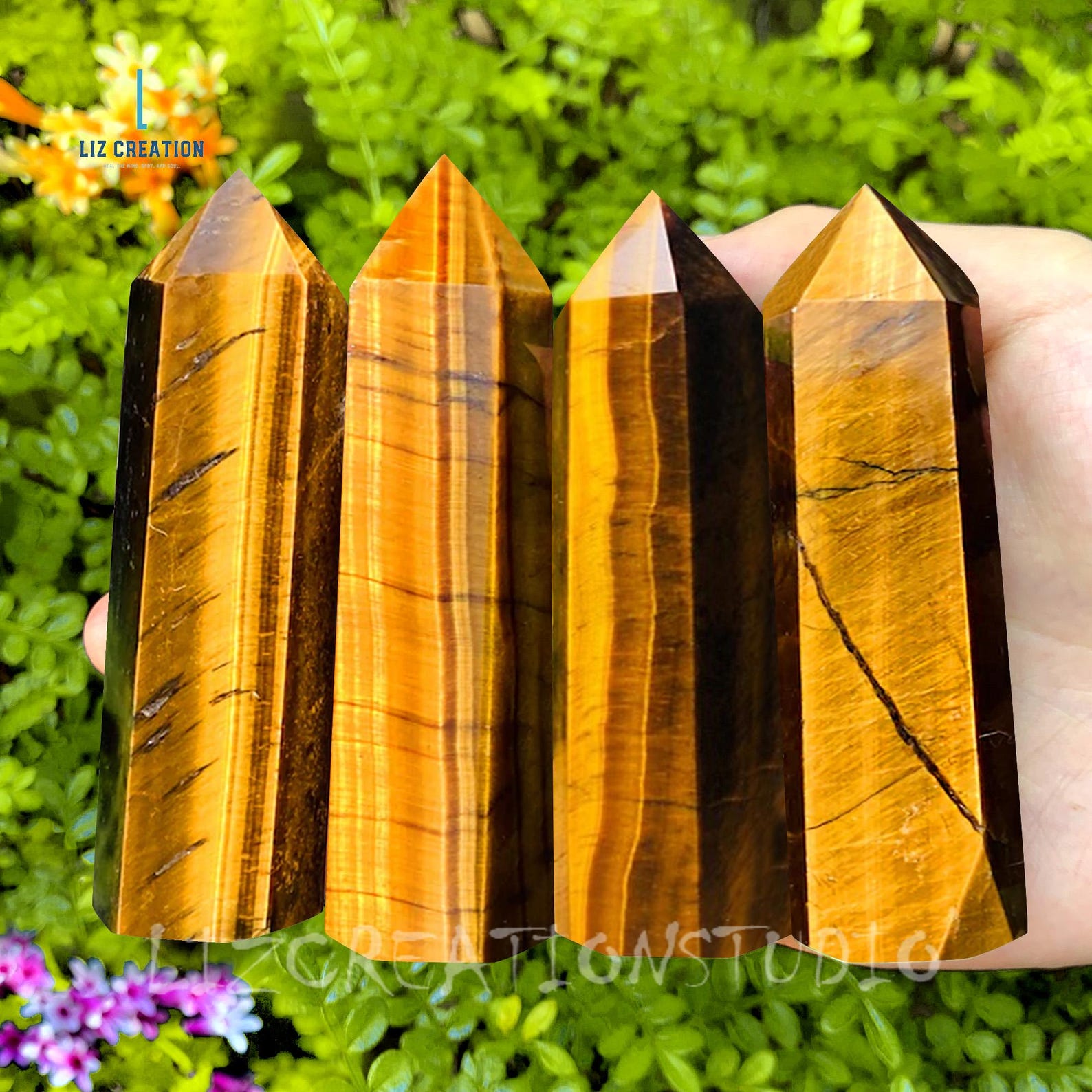Golden-brown Tiger’s Eye crystal towers held in a hand, used for Taurus zodiac energy, with bright green foliage in the background.