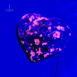 Puede incluir: Una piedra en forma de coraz&oacute;n con una base azul oscuro y vibrantes manchas rosas y moradas. La piedra est&aacute; sobre un fondo azul profundo. El texto "LIZ CREATION" est&aacute; en la esquina superior izquierda.