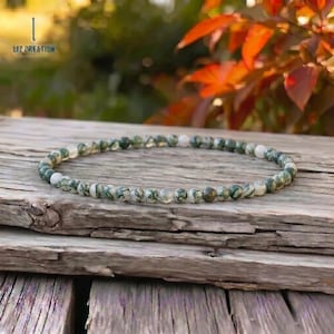 Könnte beinhalten: Ein filigranes Armband aus kleinen, runden Perlen. Die Perlen sind eine Mischung aus Grün und Weiß mit einem gesprenkelten Muster. Das Armband liegt auf einer verwitterten Holzoberfläche. Der Text "LIZ CREATION" ist zu sehen.