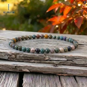 Könnte beinhalten: Ein Armband aus kleinen, runden Edelsteinen in den Farben Grün, Braun, Lila und Rosa. Das Armband liegt auf einer verwitterten Holzoberfläche. Der Text "LIZ CREATION" ist in der oberen linken Ecke sichtbar.