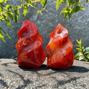 May include: Two red carnelian crystal formations with white agate banding. The crystals are freeform and have a rough, natural texture.