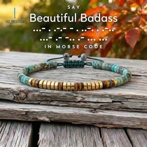 Op de afbeelding: Een armband met turquoise en goudkleurige kralen. De armband ligt op een houten oppervlak. De tekst op de afbeelding luidt "Beautiful Badass" in morsecode.