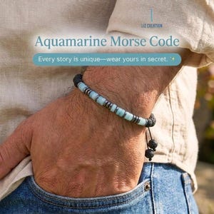 May include: A bracelet featuring light blue aquamarine beads interspersed with small dark metallic spacers and black lava stone beads. The design includes a dangling cord end with two black lava stone beads. Text reads Aquamarine Morse Code.