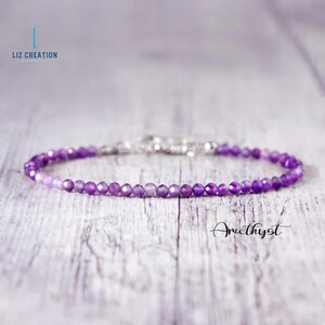 May include: A delicate amethyst bracelet with small, faceted beads. The bracelet is a deep purple color and has a silver clasp. The word "Amethyst" is written in cursive script. The brand name "Liz Creation" is also visible.