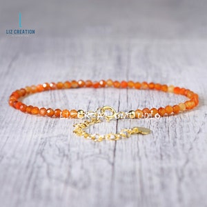 May include: A delicate orange carnelian gemstone bracelet with a gold clasp and extender chain. The bracelet is made with small, faceted beads and is perfect for layering with other bracelets.