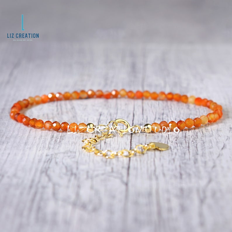 May include: A delicate orange carnelian gemstone bracelet with a gold clasp and extender chain. The bracelet is made with small, faceted beads and is perfect for layering with other bracelets.