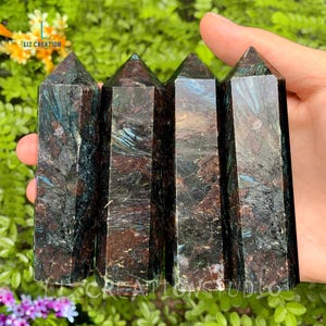May include: Four dark green and brown crystal points with a metallic sheen. The points are arranged vertically in a row, held in a hand.