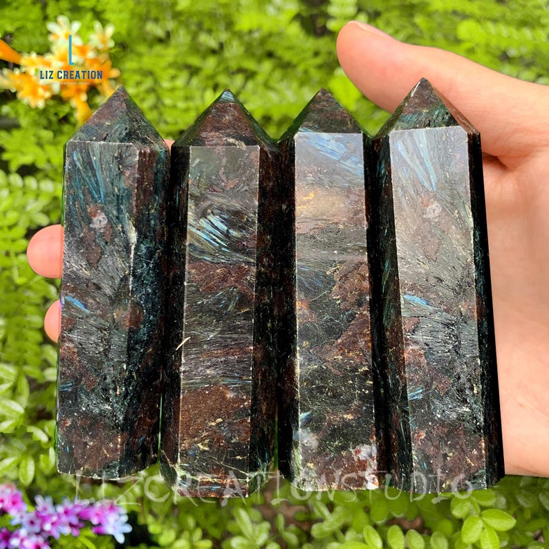 May include: Four dark green and brown crystal points with a metallic sheen. The points are arranged vertically in a row, held in a hand.