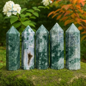 May include: Five green and white agate crystal obelisks with pointed tops are displayed on a mossy surface. The crystals vary in pattern and color, with one showing a hollow center. The background features greenery and the text "LIZ CREATION".