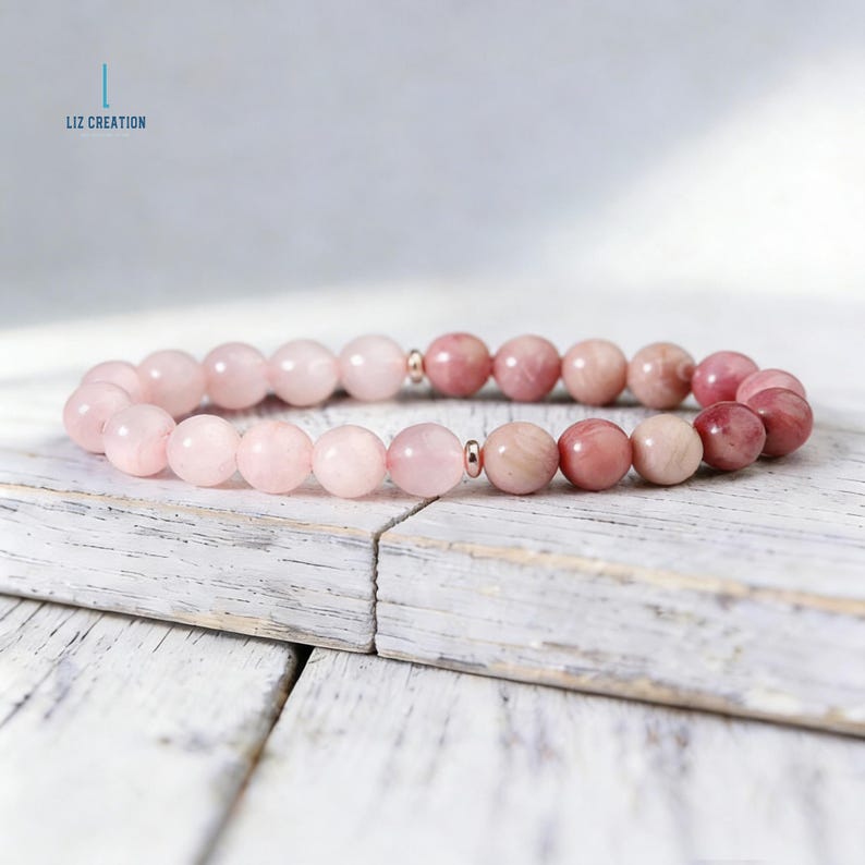 Puede incluir: Un brazalete de cuentas con piedras preciosas rosas y rosadas. El brazalete tiene peque&ntilde;os detalles met&aacute;licos y se muestra sobre una superficie de madera blanca y desgastada. El texto "LIZ CREATION" es visible en la esquina superior izquierda.