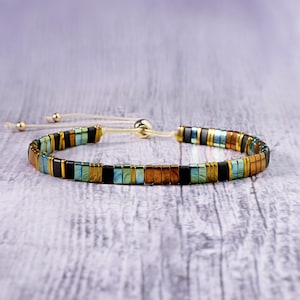 Op de afbeelding: Een veelkleurige kralen armband met een schuifknoop sluiting. De armband heeft een mix van zwarte, gouden en blauwe kralen.