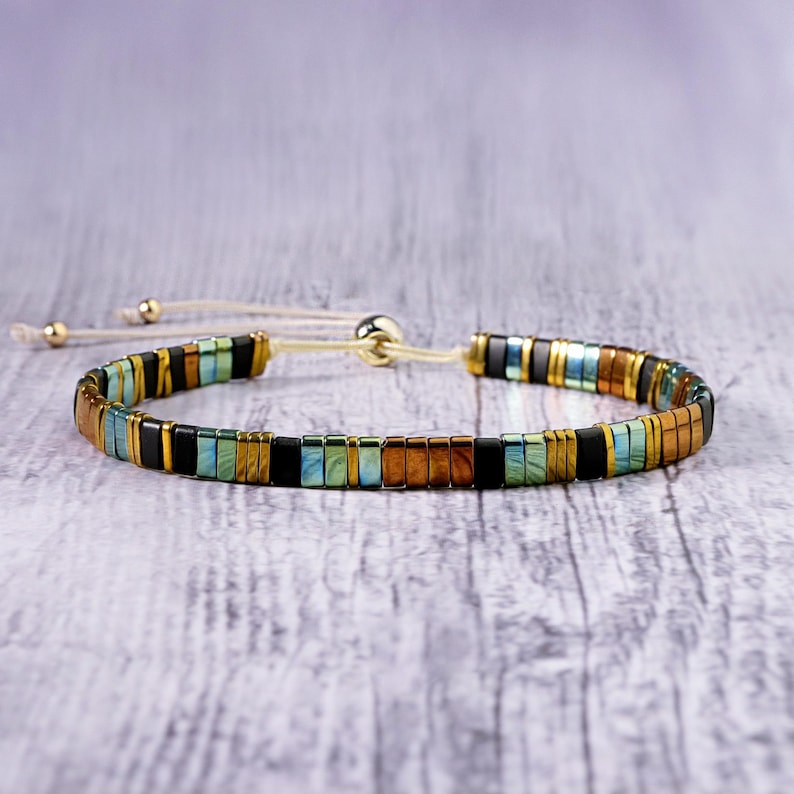 Op de afbeelding: Een veelkleurige kralen armband met een schuifknoop sluiting. De armband heeft een mix van zwarte, gouden en blauwe kralen.