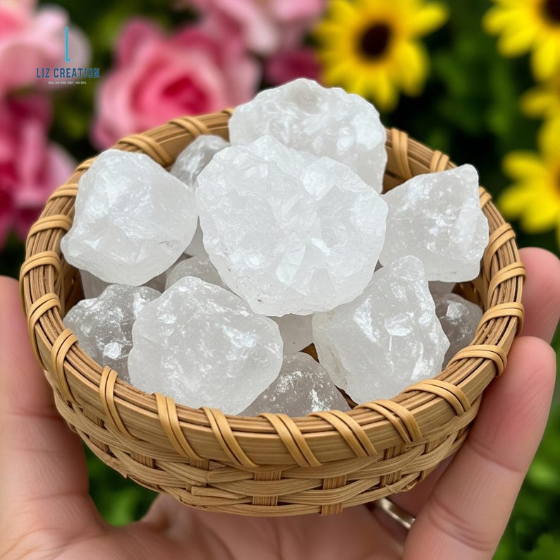 Op de afbeelding: Een klein, geweven mandje gevuld met verschillende grote, onregelmatig gevormde, witte kwartskristallen. Het mandje wordt in een hand gehouden, met een vage achtergrond van roze rozen en gele bloemen.