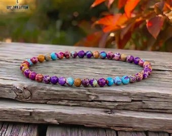 May include: A beaded bracelet featuring a variety of colorful gemstones. The bracelet includes purple, blue, orange, and red beads. The bracelet is displayed on a weathered wooden surface. The text "LIZ CREATION" is visible in the upper left corner.