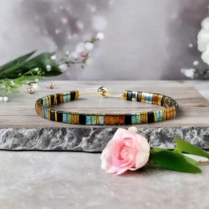 Op de afbeelding: Een veelkleurige kralen armband met een gouden sluiting. De armband heeft zwarte, bruine, groene en blauwe kralen.