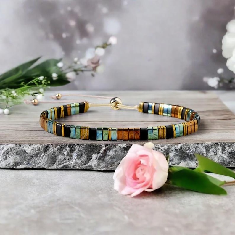 Op de afbeelding: Een veelkleurige kralen armband met een gouden sluiting. De armband heeft zwarte, bruine, groene en blauwe kralen.