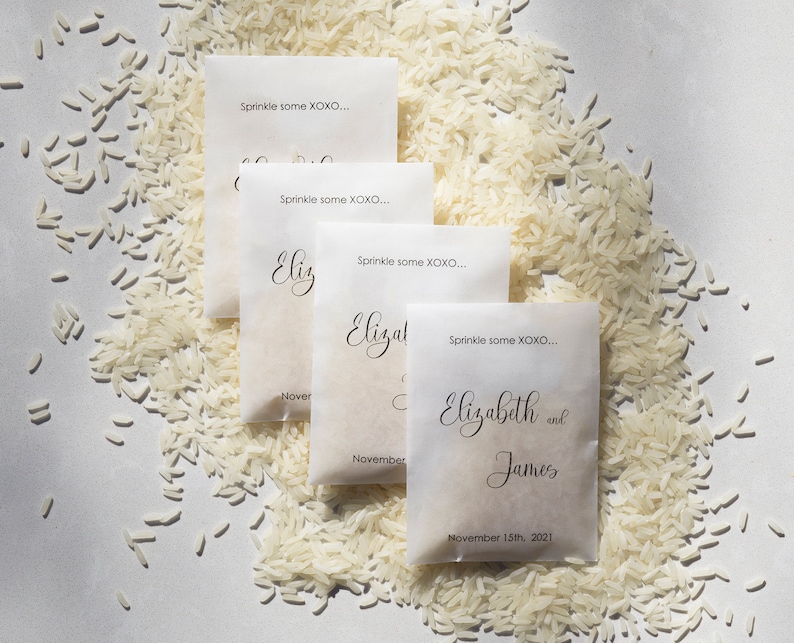 May include: Four white paper bags with black text. The bags are filled with white rice. The text on the bags reads "Sprinkle some XOXO..." and includes the names "Elizabeth and James" and the date "November 15th, 2021".