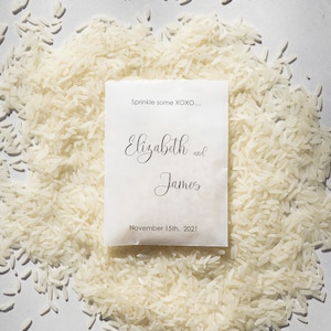 May include: White paper bag with the text "Sprinkle some XOXO..." and "Elizabeth and James" with the date "November 15th, 2021". The bag is surrounded by white rice.
