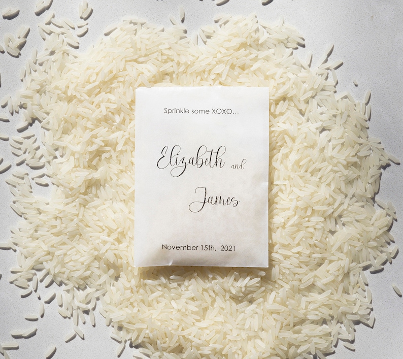 May include: White paper bag with the text "Sprinkle some XOXO..." and "Elizabeth and James" with the date "November 15th, 2021". The bag is surrounded by white rice.