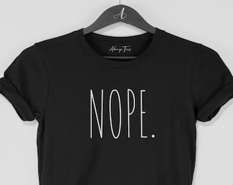 May include: Black t-shirt with the word "NOPE." in white, sans-serif font. The shirt is hanging on a black hanger. The brand name "Always Tees" is printed on the hanger.
