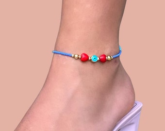Puede incluir: Un brazalete de tobillo azul con cuentas de corazón rojas y una cuenta turquesa de ojo turco.