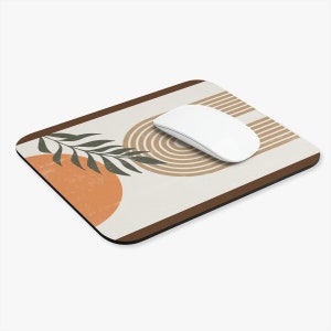 May include: A beige mouse pad with a brown border features an abstract design with a green leaf, orange and brown circles, and brown stripes. A white computer mouse is on the pad.