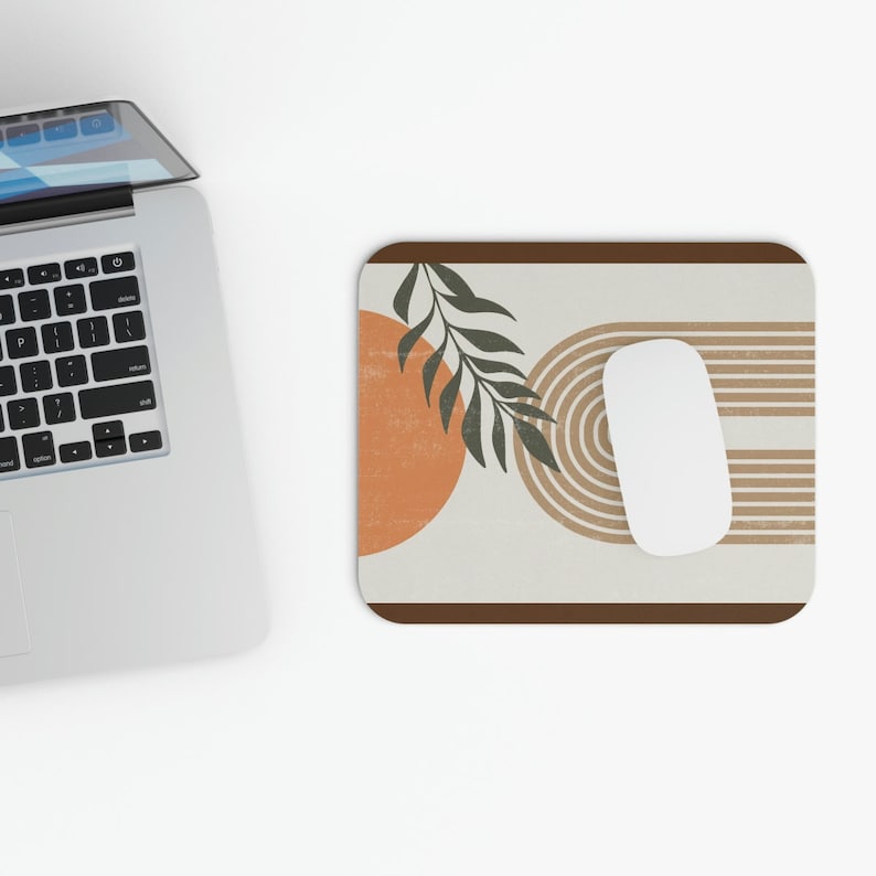 May include: A beige mouse pad with a brown border features an abstract design with an orange circle, brown stripes, and a green leaf.