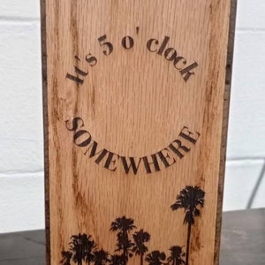 May include: Wooden sign with the text "It's 5 o'clock somewhere" in a circle with palm trees at the bottom.