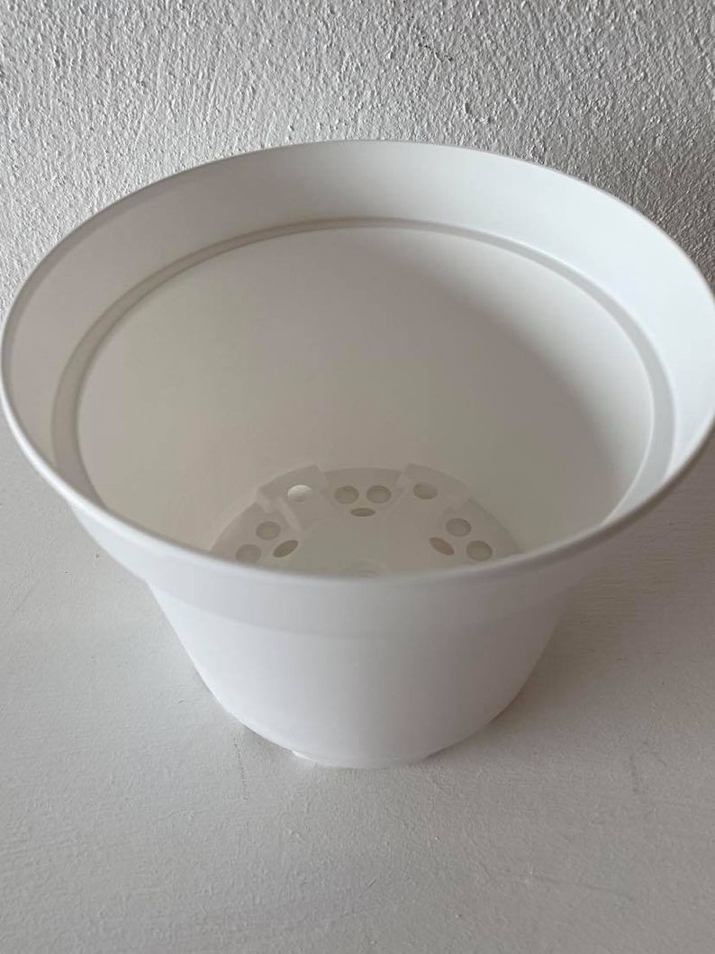 Op de afbeelding: Een witte plastic plantenpot met drainagegaten in de bodem. De pot is leeg en klaar om te planten.
