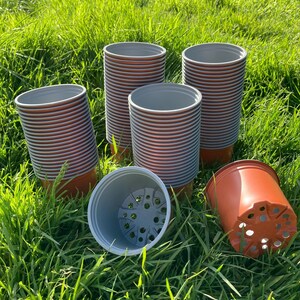 May include: A collection of terracotta-coloured plastic plant pots with grey interiors. Several pots are stacked vertically in columns, while two additional pots are positioned horizontally, revealing the drainage holes at the base.