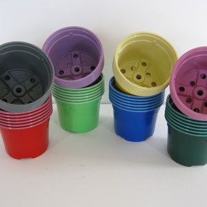 May include: Six stacks of plastic plant pots in different colours. The stacks are arranged in a row from left to right: grey, purple, green, blue, pink, and green. Each stack has a different colour pot on top.