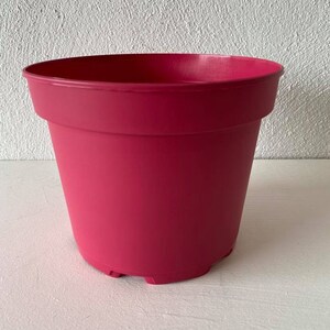Op de afbeelding: Een felroze plastic bloempot met een afgeronde bodem en een licht uitlopende rand.