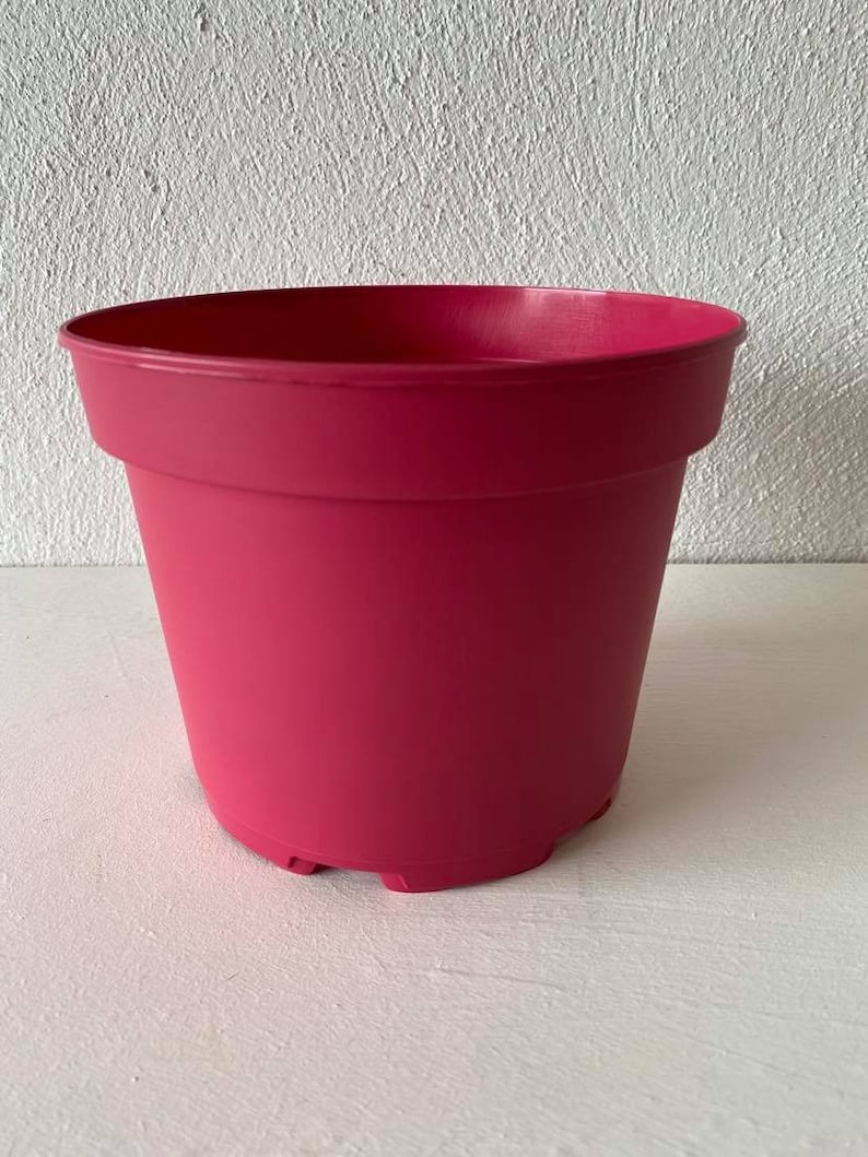 Op de afbeelding: Een felroze plastic bloempot met een afgeronde bodem en een licht uitlopende rand.