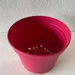 Op de afbeelding: Een felroze plastic bloempot met drainagegaten in de bodem.