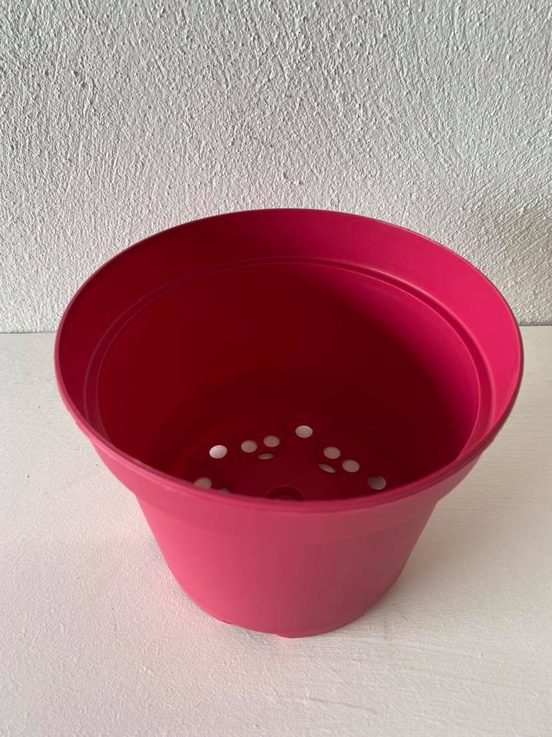 Op de afbeelding: Een felroze plastic bloempot met drainagegaten in de bodem.