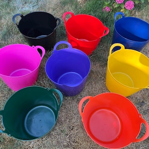 May include: A collection of eight flexible plastic tubs in various solid colours including black, red, blue, pink, purple, yellow, dark green, and orange. Each round container features two integrated handles on opposite sides for easy carrying.