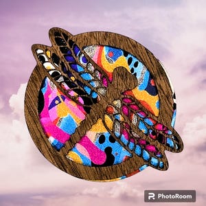 May include: A wooden round ornament with a colorful abstract design and a cutout of a bird in flight. The ornament is painted in shades of pink, blue, yellow, and black.