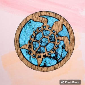 May include: A round wooden coaster with a blue and black geometric design. The design is reminiscent of a snowflake or a starburst.