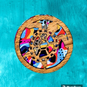 May include: A round wooden coaster with a colorful abstract design featuring swirls, dots, and geometric shapes in shades of blue, pink, yellow, red, and black.