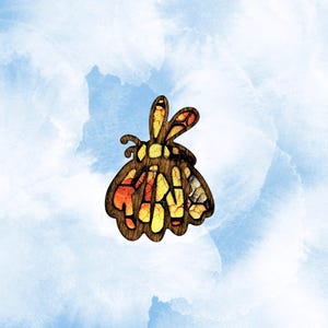 May include: A wooden butterfly-shaped pendant with a stained glass design. The pendant features a brown outline with orange, yellow, and red segments. The background is a watercolor wash of blue and white.
