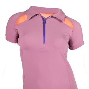 Pode incluir: Uma camisa de manga curta de cor malva com z&iacute;per roxo e pain&eacute;is de malha laranja nos ombros.