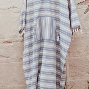 Op de afbeelding: Een blauw-wit gestreepte hooded handdoek met een zak en franjes.