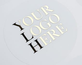 May include: A circular, semi-transparent sticker featuring the text "YOUR LOGO HERE" printed in a bold, dark serif font. The sticker has a smooth, matte finish and is positioned against a plain, light-colored background, highlighting the typography.