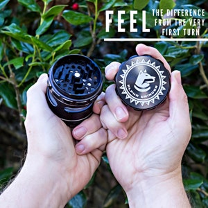 May include: A black metal grinder with a silver top. The top has a white logo that says "Alpha Grinder" with a dog head inside a starburst. The text "Feel the difference from the very first turn" is in white text on a black background.