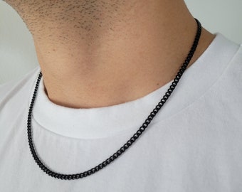 May include: A black chain necklace on a person's neck. The chain is a curb chain style.